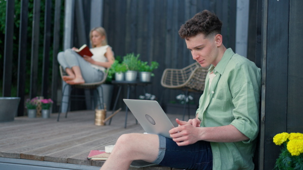 A happy young couple with laptop resting outdoors in a tiny house, weekend away and remote office concept.