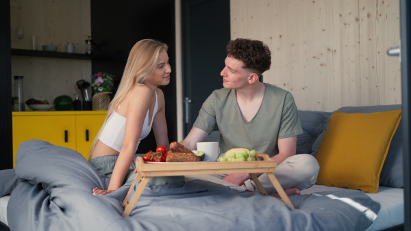 A young beautiful couple in love is sitting in bed and having healthy breakfast together.