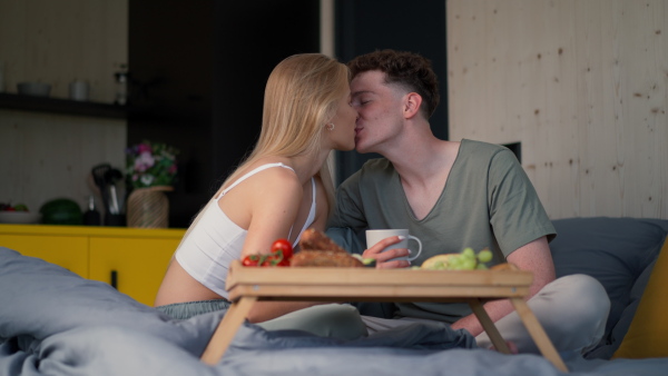 A young beautiful couple in love is sitting in bed and having healthy breakfast together.