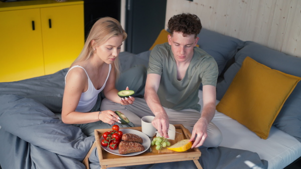 A young beautiful couple in love is sitting in bed and having healthy breakfast together.