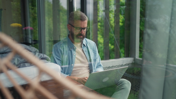 A mature man using laptop and working in tiny house, in front of nature. Freelancer office concept