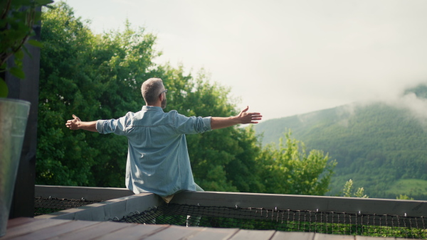 A mature man sitting in tiny house terrace. Enjoying freedom, nature and summer time. Rear view.