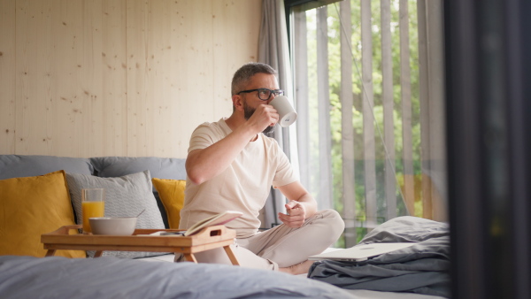 A mature man having breakfast and working in tiny house, in front of nature. Freelancer office concept