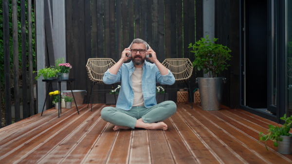 A mature man sitting in terrace, listening music with headphones and enjoying summer time.