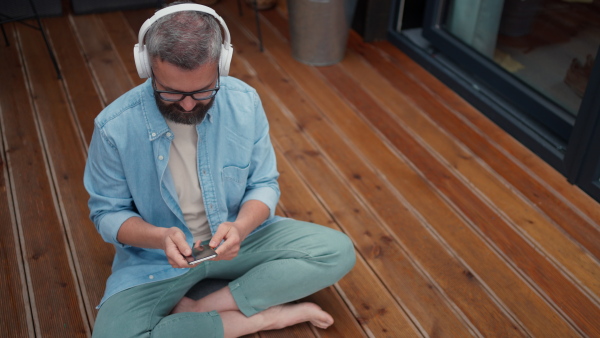 High angle view of mature man listening music while using smart phone at wooden terrace.