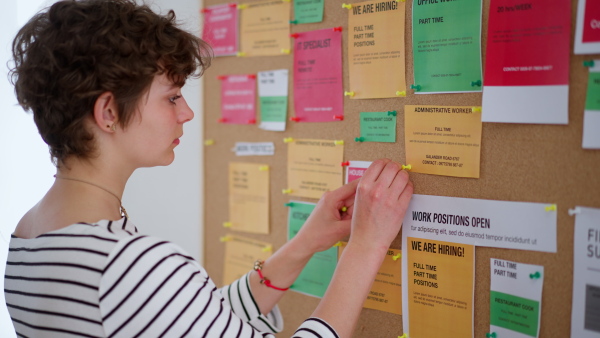 A job center employee pinning job vacancies on employment noticeboard.