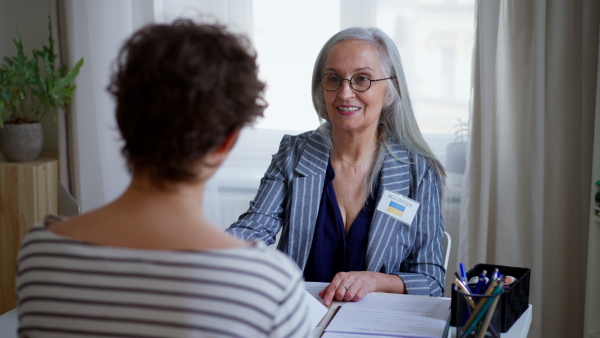 A senior woman volunteer helping Ukrainian woman to fill in forms at asylum centre.