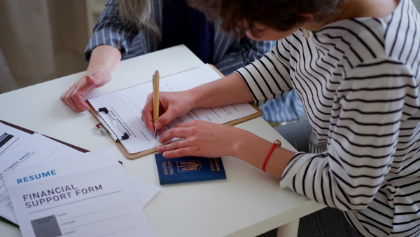 A senior woman volunteer helping Ukrainian woman to fill in forms at asylum centre.