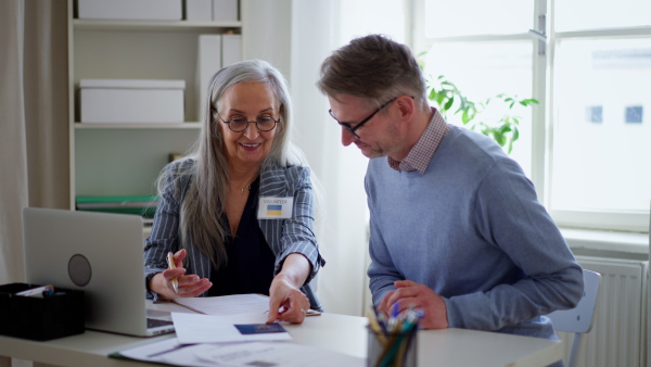 A senior woman volunteer helping Ukrainian man to fill in forms at immigration office.