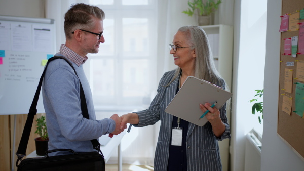 A recrutiment agency employee standing in front of employment noticeboard and helping mature man search for a job.