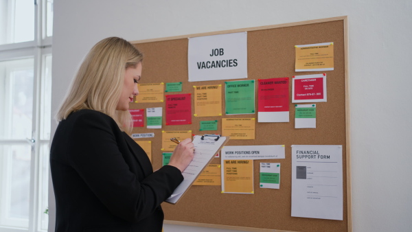 A job center employee with file form standing in front of employment noticeboard.