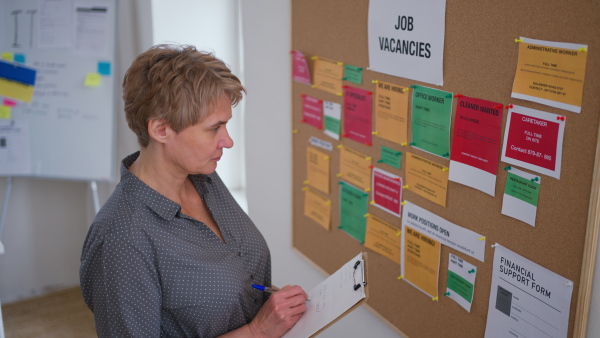 A job center employee with file form standing in front of employment noticeboard.