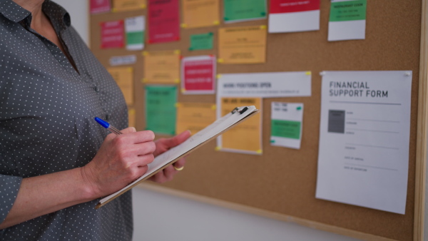 A job center employee with file form standing in front of employment noticeboard.