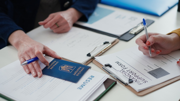 A senior woman volunteer helping Ukrainian woman to fill in forms at asylum centre.