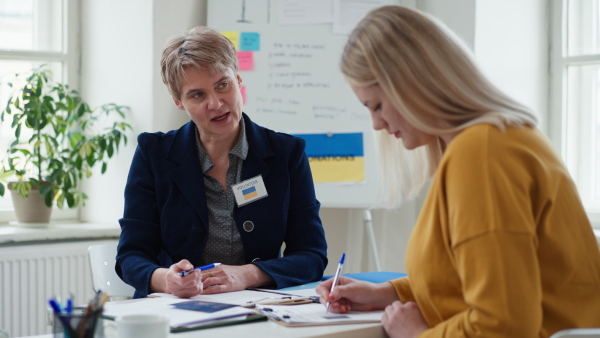 A senior woman volunteer helping Ukrainian woman to fill in forms at asylum centre.