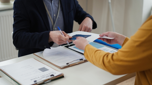 A man volunteer helping Ukrainian woman to fill in forms at asylum centre, close-up