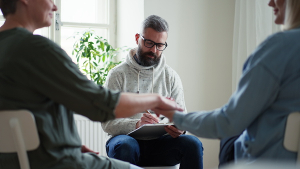 A therapist with people communicating while sitting in circle and talking, group therapy.