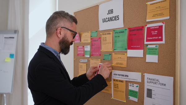 A job center employee pinning job vacancies on employment noticeboard.