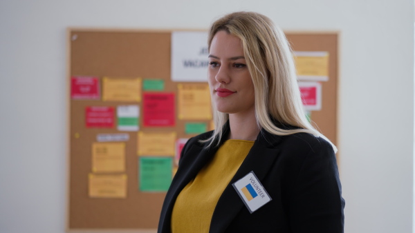 A happy young woman student standing in front of employment noticeboard, looking at camera.