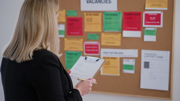 A job center employee with file form standing in front of employment noticeboard.