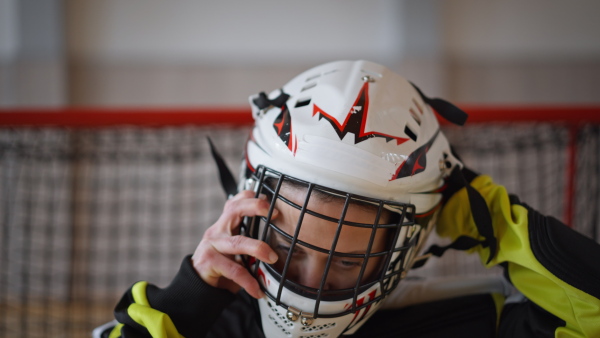 A close-up of woman floorball goalkeeper putting on helmet and preapring for game in gym.