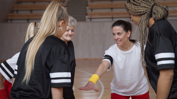 A group of young and old women in gym stacking hands together, sport team players.