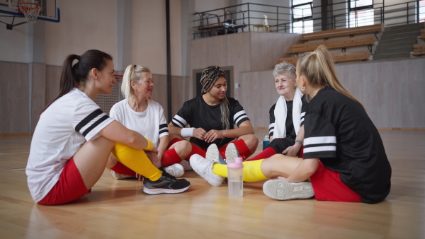 Group of young and old women, sports team players in gym sitting and talking after match.