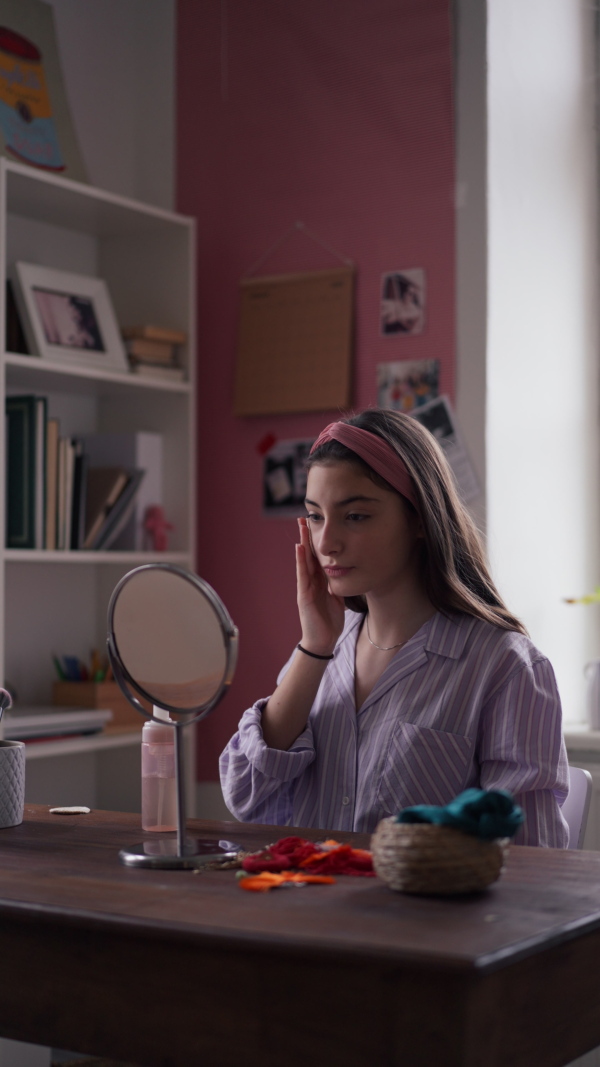 Vertical view of a teenage girl doing her skin care routine in the room.