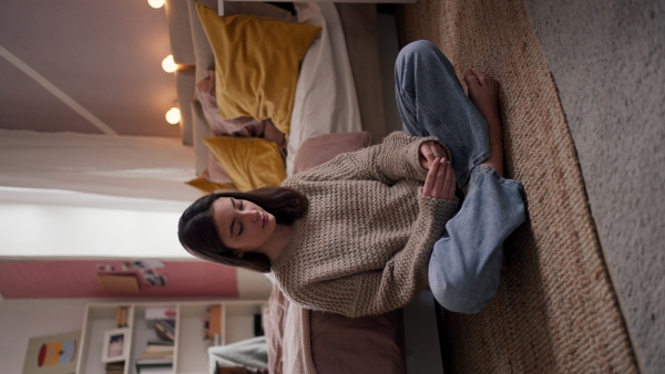 Vertical view of a sad teenage girl sitting on the floor in her room.