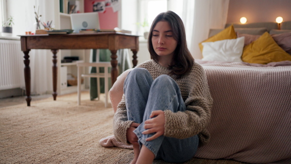 Sad teenage girl sitting on the floor in her room.