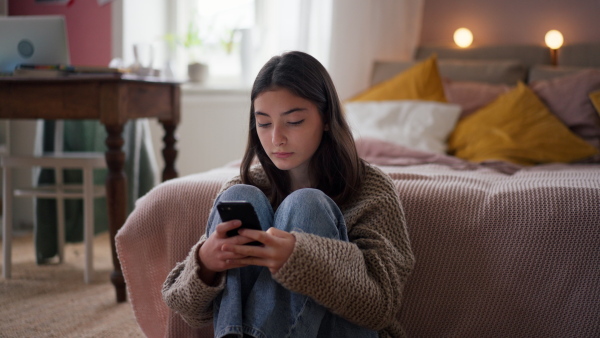 Young teenage girl srolling her smartphone in a room.