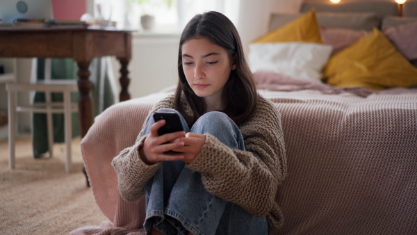 Young teenage girl srolling her smartphone in a room.