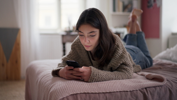 Young teenage girl srolling her smartphone in a room.