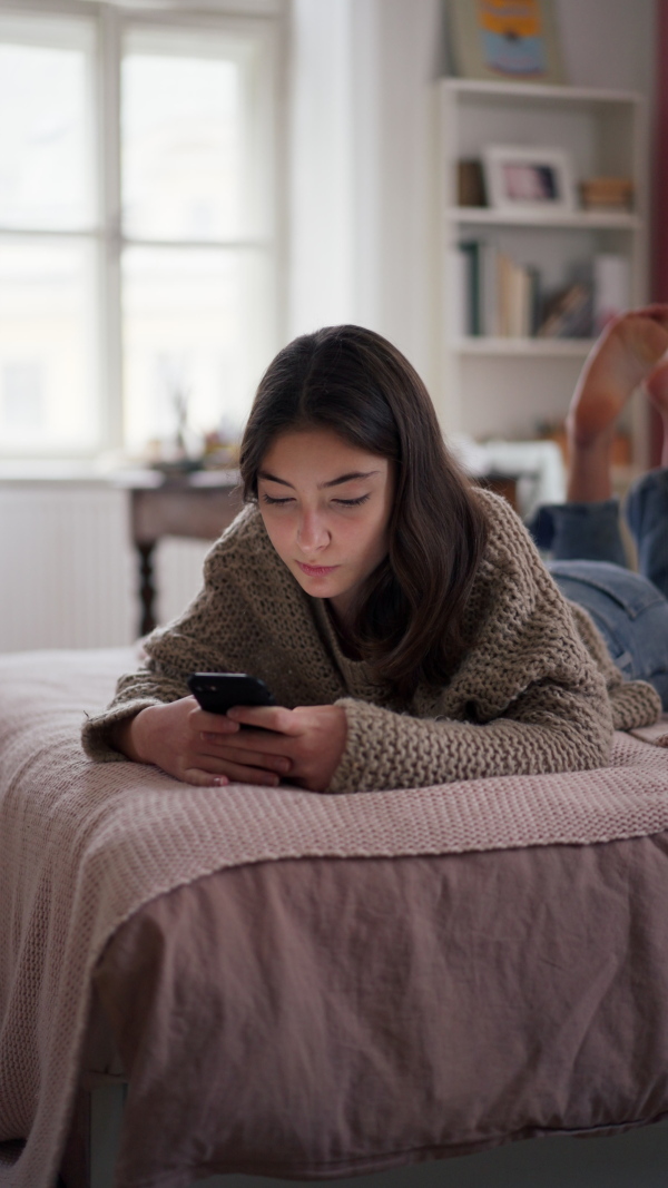 Vertical view of a young teenage girl srolling her smartphone in a room.