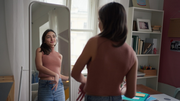 A young teenage girl looking in the mirror in the room, trying on clothes and dancing.