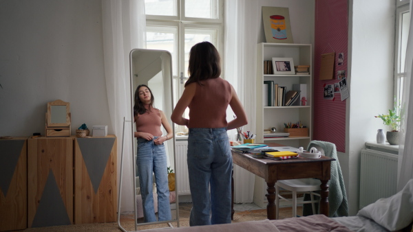 A young teenage girl looking in the mirror in the room, trying on clothes.