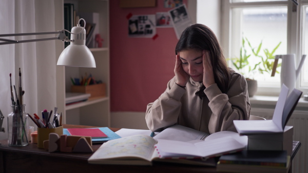 Young teenage girl studying and doing homework in her room, having a mental breakdown.