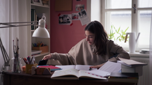 Young teenage girl studying in her room and scrolling smartphone.