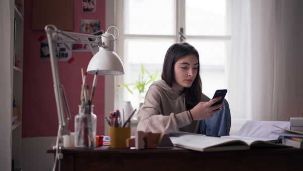 Young teenage girl having a break from studying and scrolling smartphone.