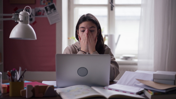 Young teenage girl studying in her room, having a problems with homework.