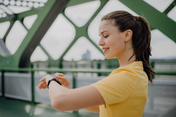 Young woman checking a smartwatch in city, preparing for run, healthy lifestyle and sport concept.