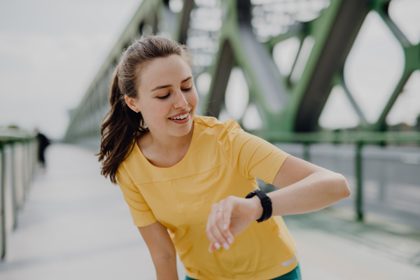 Young woman checking a smartwatch in city, preparing for run, healthy lifestyle and sport concept.