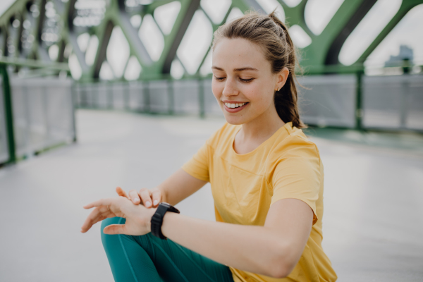 Young woman checking a smartwatch in city, preparing for run, healthy lifestyle and sport concept.