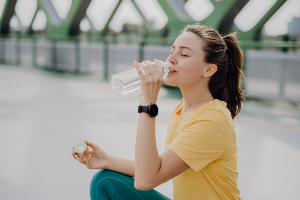 Young woman drinking water during jogging in a city, healthy lifestyle and sport concept.