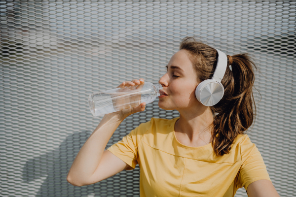 Young woman drinking water and listening music during jogging in a city, healthy lifestyle and sport concept.