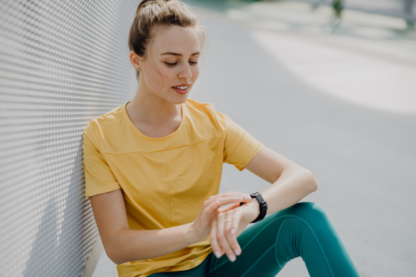 Young woman checking a smartwatch in city, preparing for run, healthy lifestyle and sport concept.