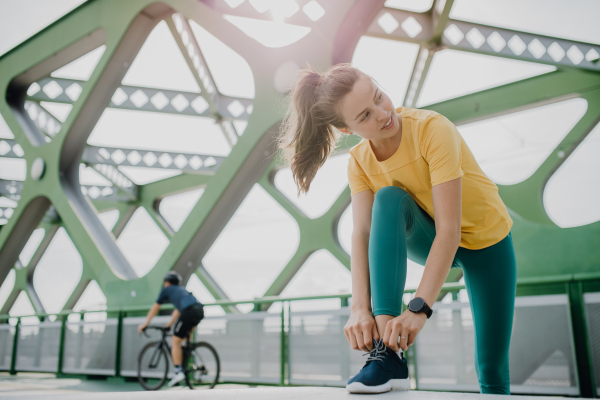 Portrait of young sportive woman resting outdoor in a city during running, tiing her shoelaces.