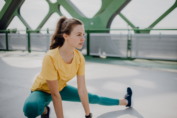 Young woman doing stretching in a city, preparing for run, healthy lifestyle and sport concept.