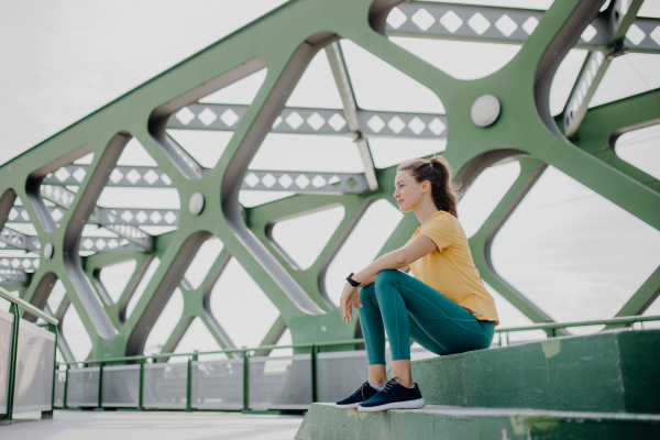 Young sportive woman resting after run, outdoor in a city.