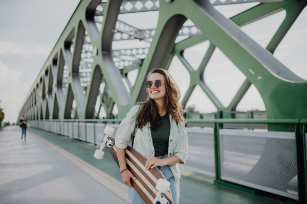 Young woman walking on city bridge with a skateboard. Youth culture and commuting concept.